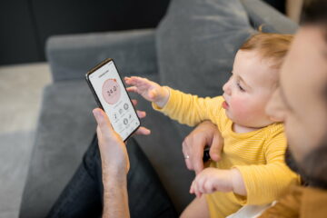 Father with a baby controlling home devices by smartphone