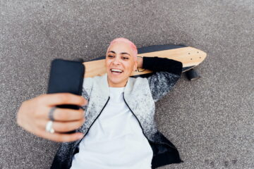 Skateboarder lying on board and using phone