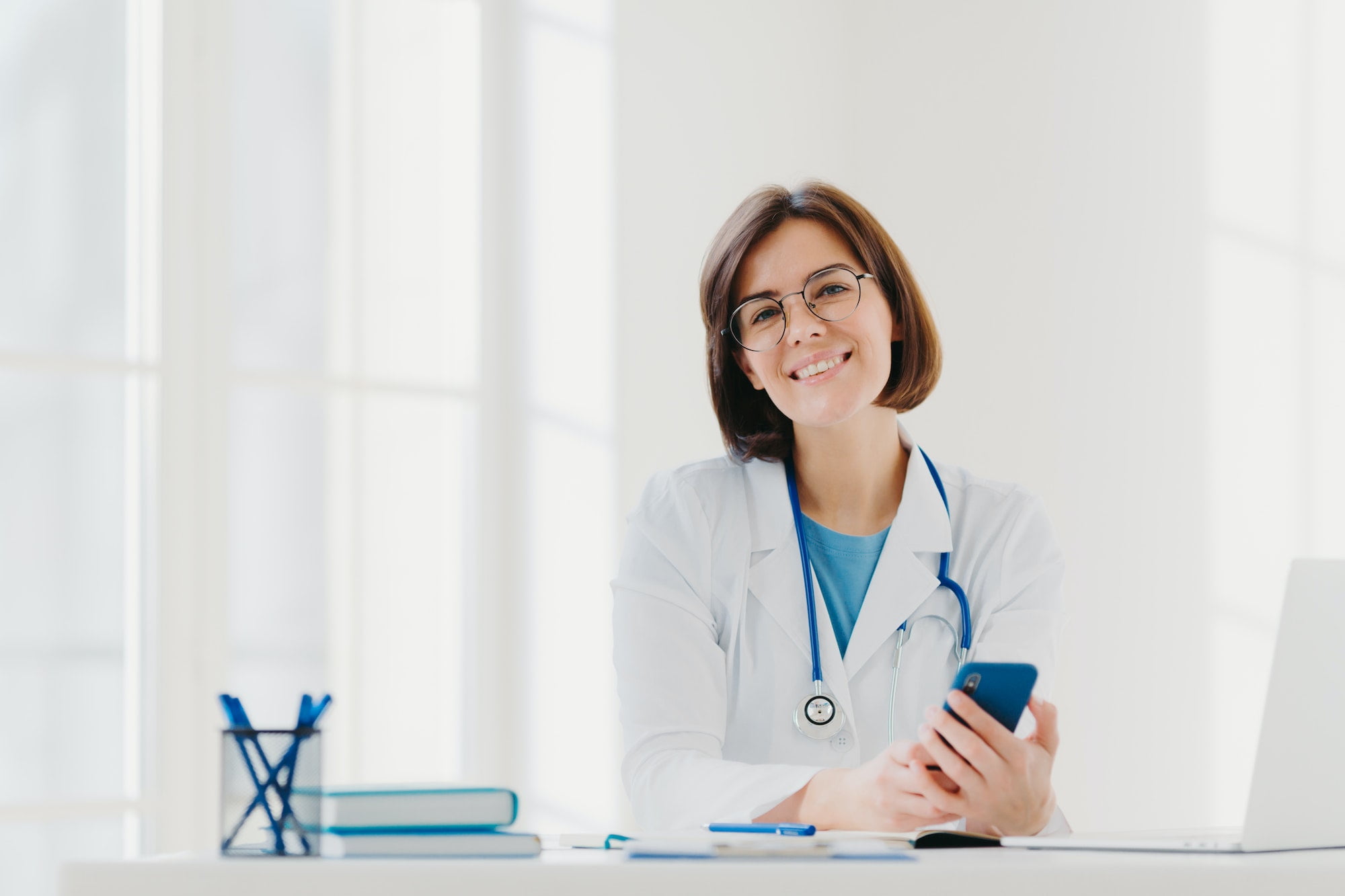 Smiling professional doctor works in clinic, poses at modern hospital office with electronic gadgets