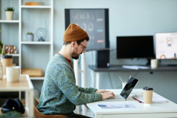 Young male employee or designer sitting in front of laptop and networking