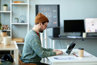 Young male employee or designer sitting in front of laptop and networking