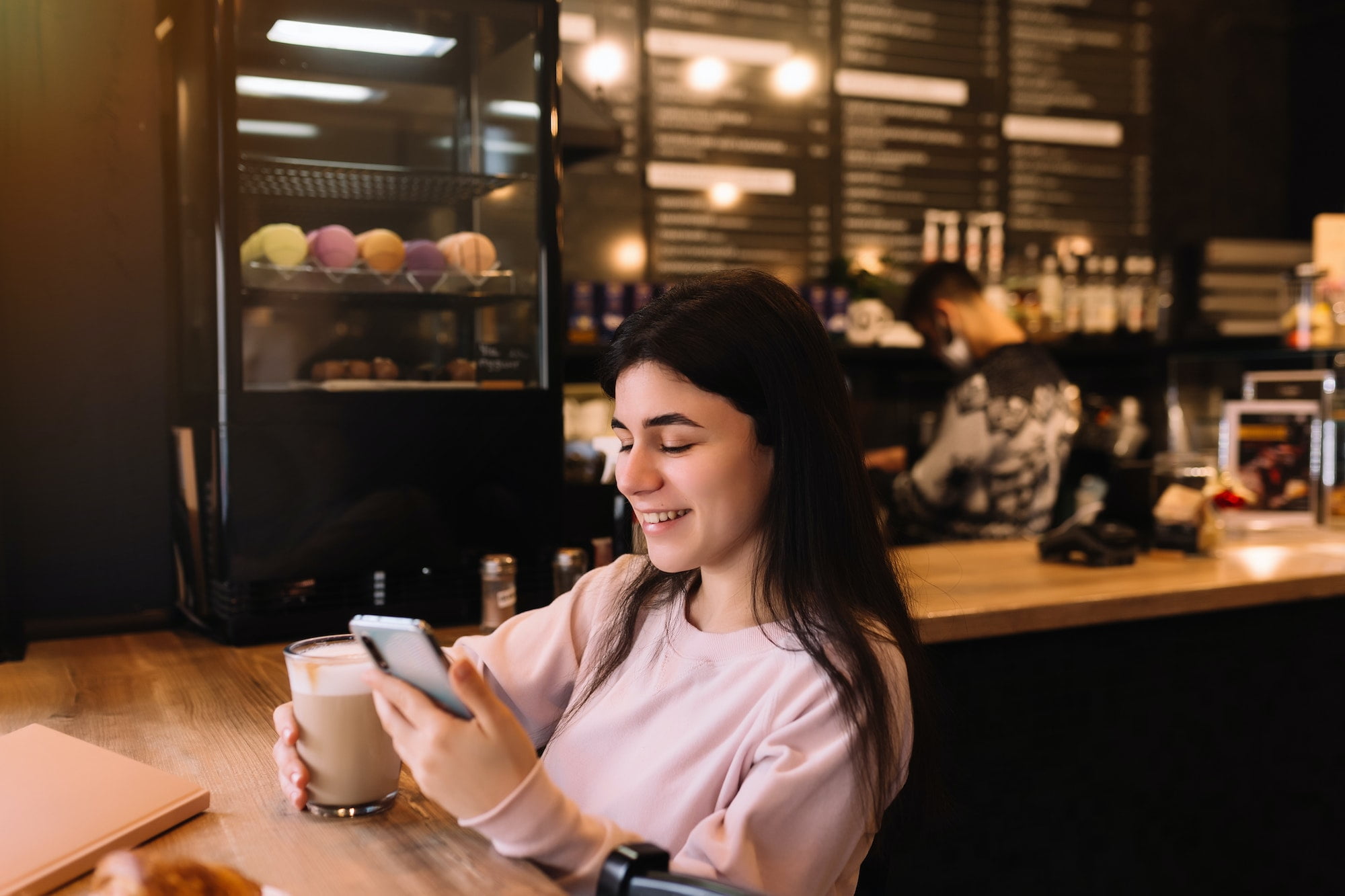 Girl smiling, drinks coffee in cafe and reading phone. Blurred background