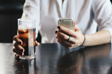 The girl writes the message on the iPhone and drinks Coca-Cola