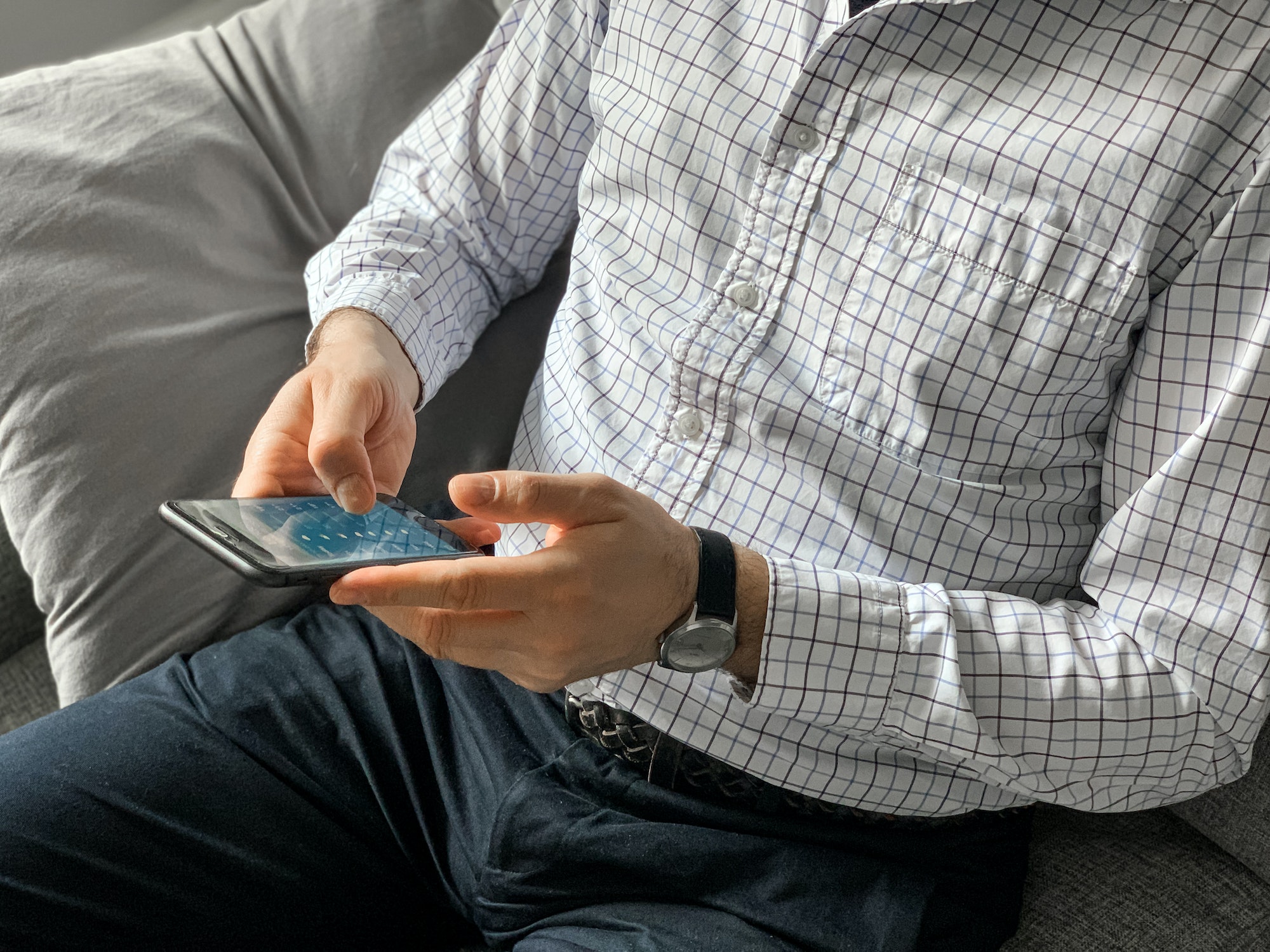 Man sitting on sofa at home before going to office and using smartphone to check weather forecast