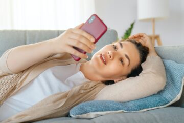 woman is using a phone sitting on a sofa