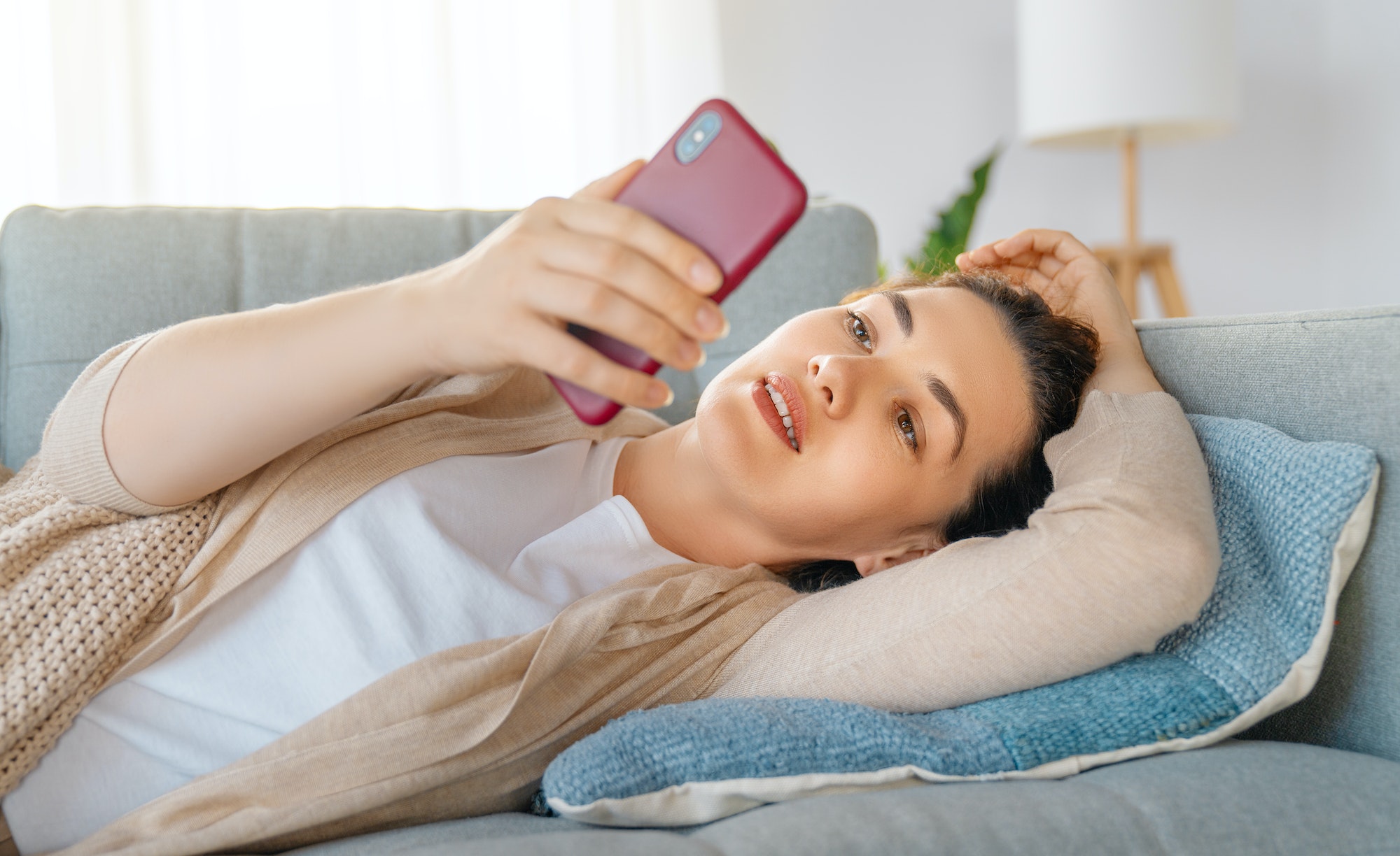 woman is using a phone sitting on a sofa