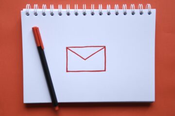 Overhead photo of a notebook with a drawing of a symbol for email and a pen on red background